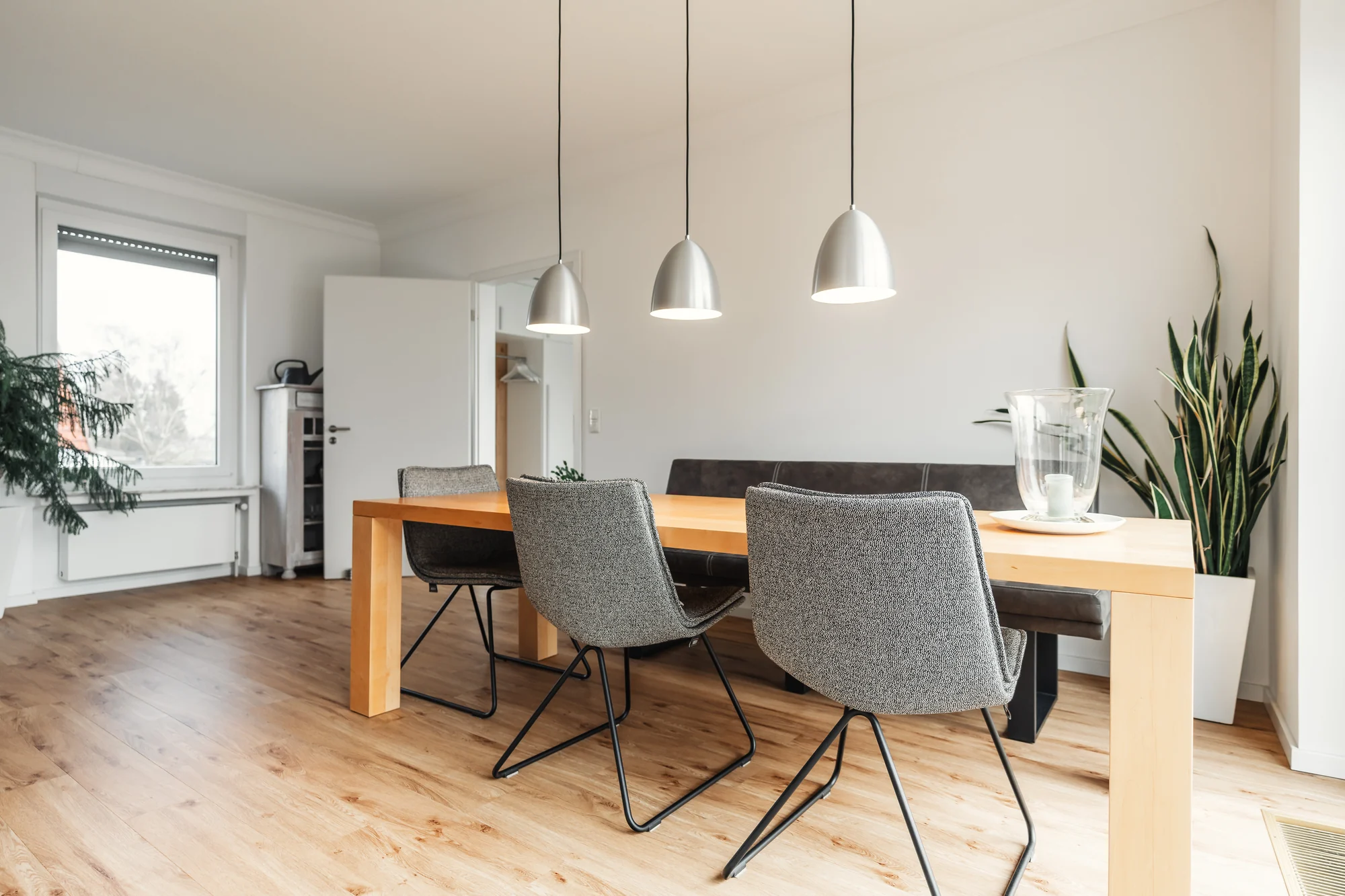 Heller Essbereich mit Holztisch, grauen Polsterstühlen und drei Pendelleuchten